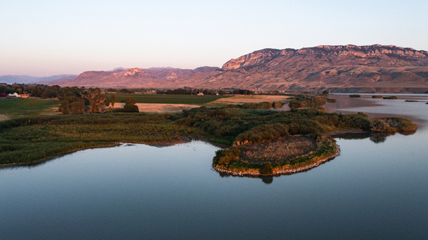 Aerial view of the landscape near the lake with lush green wetlands and rugged mountains in the background during golden hour in Cody Wyoming United States.