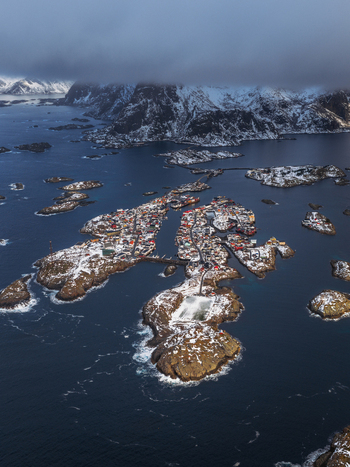 Aerial view of snow dusted rooftops huddle together on the isles surrounded by the dark swirling waters of the Norwegian Sea Henningsv&aelig;r Nordland Norway.