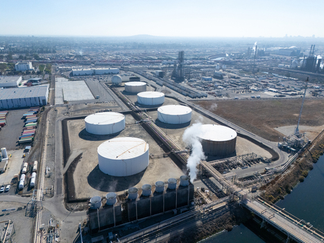 Aerial view of an industrial facility featuring large white storage tanks cooling towers emitting steam and surrounding infrastructure in Carson California United States.
