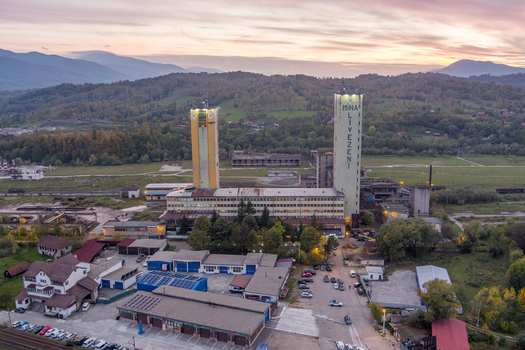 Aerial view of Mina Livezeni coal mine with tall industrial towers mine buildings and parking area nestled against rolling hills at sunset in Petrosani Judetul Hunedoara Romania. Aerial view of Mina Livezeni coal mine with tall industrial towers mine buildings and parking area nestled against rolling hills at sunset in Petrosani Judetul Hunedoara Romania.