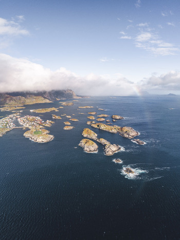 Aerial view of the Lofoten archipelago featuring rugged rocky islands surrounded by deep blue sea under a cloudy sky in Leknes Nordland Norway. Aerial view of the Lofoten archipelago featuring rugged rocky islands surrounded by deep blue sea under a cloudy sky in Leknes Nordland Norway.