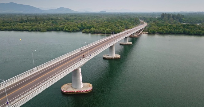 Aerial view of a long concrete bridge spanning over a calm river surrounded by lush mangrove forests under a hazy sky Thailand. Aerial view of a long concrete bridge spanning over a calm river surrounded by lush mangrove forests under a hazy sky Thailand.
