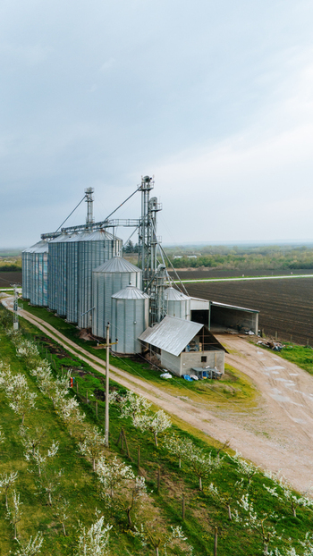 Aerial view of towering grain silos gleaming under a cloudy sky juxtaposed with vibrant green fields and bare earth Sremska Mitrovica Vojvodina Serbia. Aerial view of towering grain silos gleaming under a cloudy sky juxtaposed with vibrant green fields and bare earth Sremska Mitrovica Vojvodina Serbia.