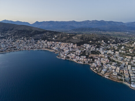 Aerial view of the coastal city featuring dense urban development along the Ionian Sea and rugged mountains in the background in Saranda Vlore County Albania. Aerial view of the coastal city featuring dense urban development along the Ionian Sea and rugged mountains in the background in Saranda Vlore County Albania.