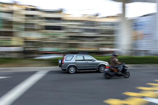 View of a grey SUV and a scooter rider moving fast through a city street with motion blur and urban buildings in the background Taipei City Taiwan. View of a grey SUV and a scooter rider moving fast through a city street with motion blur and urban buildings in the background Taipei City Taiwan.