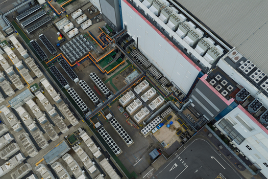 Aerial view of a large data center facility featuring rows of industrial cooling units complex HVAC systems and extensive piping networks on the roof in the United Kingdom.