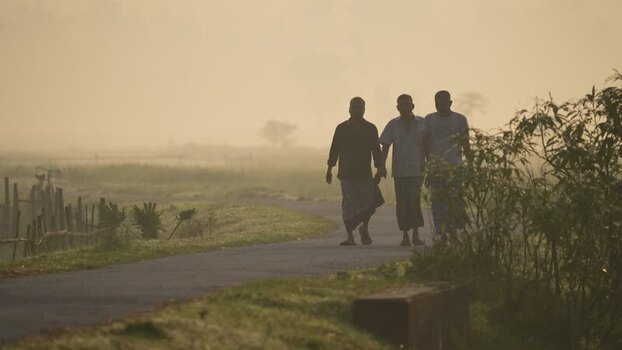 View of three men walking on a rural road through morning mist Bangladesh.