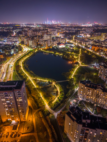 Aerial view of illuminated residential buildings surrounding a dark lake in a city park at night with the distant city skyline on the horizon in Poland. Aerial view of illuminated residential buildings surrounding a dark lake in a city park at night with the distant city skyline on the horizon in Poland.