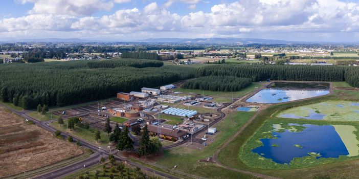 Aerial view of the wastewater treatment plant featuring circular tanks processing buildings and oxidation ponds surrounded by trees and fields in Woodburn Oregon United States. Aerial view of the wastewater treatment plant featuring circular tanks processing buildings and oxidation ponds surrounded by trees and fields in Woodburn Oregon United States.