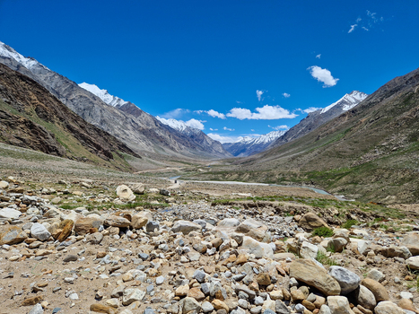 View of Penzi La road winding through the rugged Zanskar valley with snow capped Himalayan peaks rocky terrain and a clear blue sky in Zanskar Ladakh India.