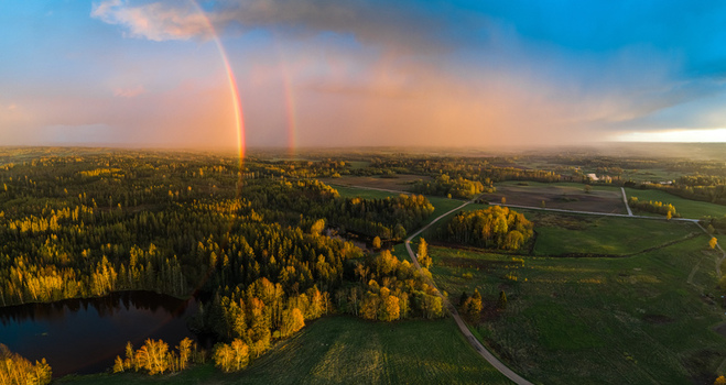 Aerial view of a double rainbow arching over a lush forest a small lake and green fields during the golden hour in Latvia. Aerial view of a double rainbow arching over a lush forest a small lake and green fields during the golden hour in Latvia.