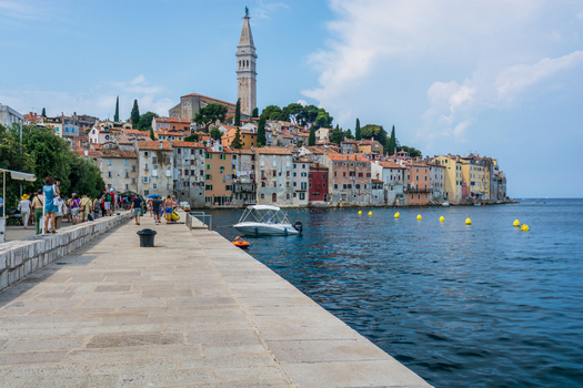 View of the historic old town of Rovinj with the Church of St. Euphemia towering over colorful waterfront buildings a stone pier and a small boat Rovinj Istria County Croatia. View of the historic old town of Rovinj with the Church of St. Euphemia towering over colorful waterfront buildings a stone pier and a small boat Rovinj Istria County Croatia.