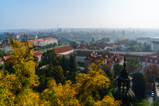 View of the historic skyline of Prague with red tiled roofs lush autumn trees and distant church spires under a hazy sky in Prague Prague Czechia.