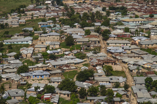 View of the dense residential area with corrugated metal roofs and dirt paths surrounded by green trees in Tiwi Wilaya ya Kwale Kenya. View of the dense residential area with corrugated metal roofs and dirt paths surrounded by green trees in Tiwi Wilaya ya Kwale Kenya.