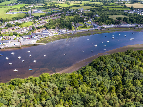 Aerial view of the River Moy flowing through Ballina with small boats moored in the water lush green trees and residential buildings along the banks in Ballina County Mayo Ireland.