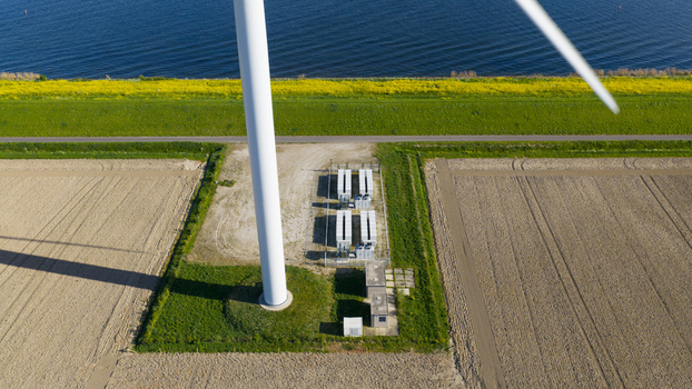 Aerial view of a wind turbine base and battery energy storage system next to agricultural fields and a coastal dike in Ooltgensplaat South Holland Netherlands. Aerial view of a wind turbine base and battery energy storage system next to agricultural fields and a coastal dike in Ooltgensplaat South Holland Netherlands.