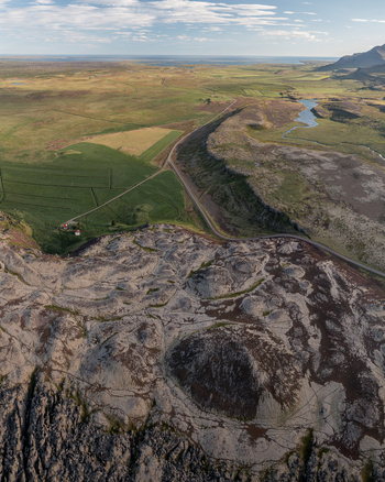 Aerial view of the volcanic crater Ytri Raudarmelskula surrounded by vast green fields rugged lava formations and a winding road in Raudhamelur Eyja og Miklaholtshr Iceland. Aerial view of the volcanic crater Ytri Raudarmelskula surrounded by vast green fields rugged lava formations and a winding road in Raudhamelur Eyja og Miklaholtshr Iceland.
