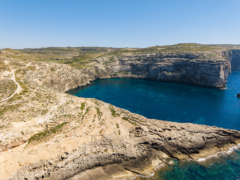 Aerial view of Dwejra Bay featuring steep limestone cliffs and deep blue Mediterranean water along the rocky coastline in Gozo Region Malta. Aerial view of Dwejra Bay featuring steep limestone cliffs and deep blue Mediterranean water along the rocky coastline in Gozo Region Malta.