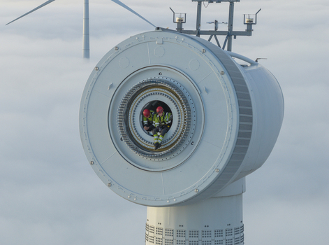 Netherlands 26 November 2025 Aerial view of two technicians in high visibility gear sitting inside a wind turbine nacelle above a thick layer of clouds. Netherlands 26 November 2025 Aerial view of two technicians in high visibility gear sitting inside a wind turbine nacelle above a thick layer of clouds.