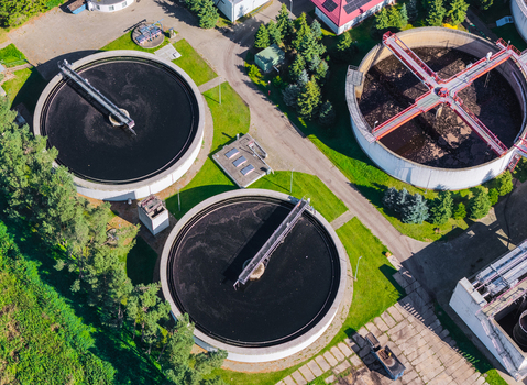 Aerial view of a wastewater treatment plant featuring large circular sedimentation tanks surrounded by green grass and industrial infrastructure in Pomeranian Voivodeshi Poland. Aerial view of a wastewater treatment plant featuring large circular sedimentation tanks surrounded by green grass and industrial infrastructure in Pomeranian Voivodeshi Poland.
