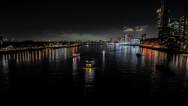 Aerial view of the River Thames at night with illuminated boats cruising past the modern skyscrapers of Canary Wharf and the city skyline in London England United Kingdom. Aerial view of the River Thames at night with illuminated boats cruising past the modern skyscrapers of Canary Wharf and the city skyline in London England United Kingdom.