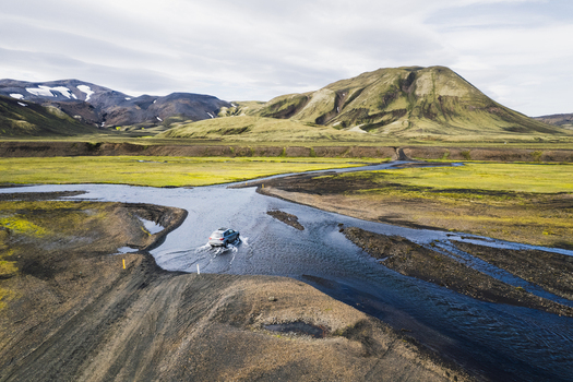 Aerial view of a vehicle crossing a shallow river on the F208 road amidst the green volcanic mountains and rugged terrain of the Highlands of Iceland Iceland. Aerial view of a vehicle crossing a shallow river on the F208 road amidst the green volcanic mountains and rugged terrain of the Highlands of Iceland Iceland.
