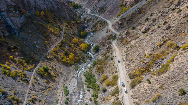 Aerial view of Sadpara Gol valley featuring a winding dirt road with vehicles a flowing stream and rugged rocky mountain slopes in Skardu Gilgit Pakistan.
