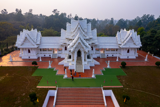 Aerial view of the white Royal Thai Monastery with its intricate tiered roofs and red tiled courtyard surrounded by lush greenery in Lumbini Nepal.