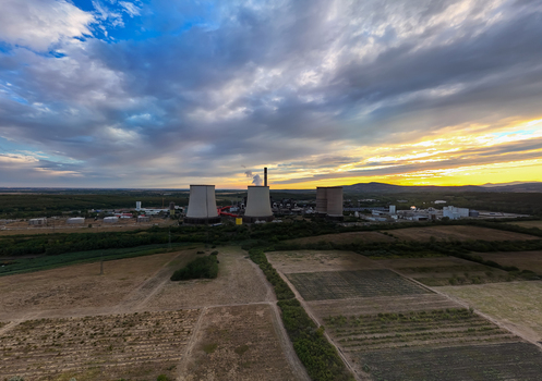 Aerial view of a lignite fired power plant with cooling towers and a smoking chimney beside cultivated fields at sunset under dramatic clouds in Visonta Hungary.