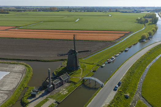 Aerial view of a traditional Dutch windmill standing beside a canal with small boats a brick pump house and vibrant tulip fields in the Netherlands. Aerial view of a traditional Dutch windmill standing beside a canal with small boats a brick pump house and vibrant tulip fields in the Netherlands.