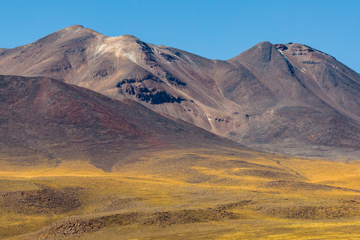 Aerial view of the Chiliques volcano rising above the arid desert landscape with volcanic slopes and golden terrain in San Pedro de Atacama Antofagasta Chile. Aerial view of the Chiliques volcano rising above the arid desert landscape with volcanic slopes and golden terrain in San Pedro de Atacama Antofagasta Chile.