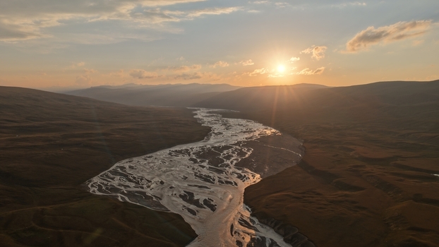 Aerial view of the Enilchek river winding through the vast mountain valley at sunset with golden light reflecting on the water in Enilchek Issyk Kul Region Kyrgyzstan. Aerial view of the Enilchek river winding through the vast mountain valley at sunset with golden light reflecting on the water in Enilchek Issyk Kul Region Kyrgyzstan.