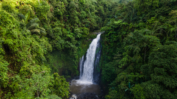 Aerial view of Gomblang Waterfall cascading through dense tropical jungle and lush green foliage in Kecamatan Kedungbanteng Jawa Tengah Indonesia. Aerial view of Gomblang Waterfall cascading through dense tropical jungle and lush green foliage in Kecamatan Kedungbanteng Jawa Tengah Indonesia.