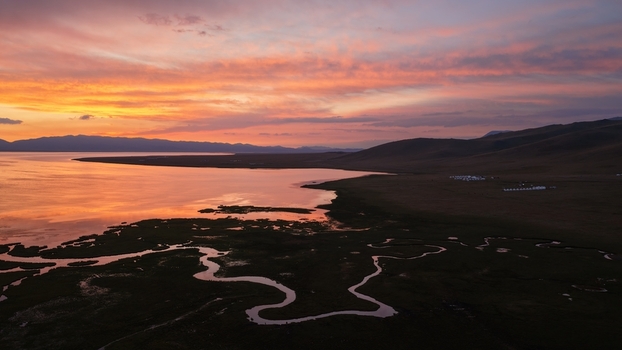 Aerial view of Song Kul lake at sunset with a winding river inlet rolling hills and vibrant orange sky reflecting on the calm water in Naryn Region Kyrgyzstan. Aerial view of Song Kul lake at sunset with a winding river inlet rolling hills and vibrant orange sky reflecting on the calm water in Naryn Region Kyrgyzstan.