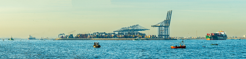 View of the busy Karachi Port with large container ships gantry cranes and shipping containers with small fishing boats in the calm waters in the foreground Karachi Sindh Pakistan.