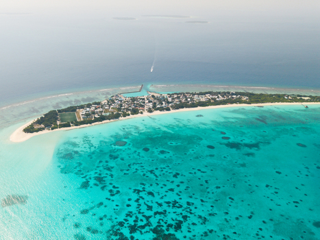Aerial view of the vibrant coral reefs contrasting with the tranquil turquoise waters surrounding the island s buildings Vashafaru Island Thiladhummathi Atoll Maldives.