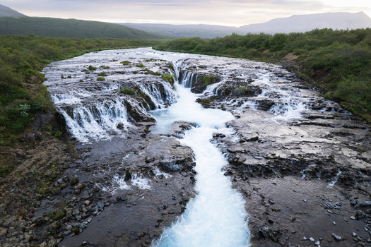 Aerial view of Bruarfoss waterfall with the turquoise water cascading over dark volcanic rock formations surrounded by lush green hills Blaskogabyggd Blaskogabyggd Iceland. Aerial view of Bruarfoss waterfall with the turquoise water cascading over dark volcanic rock formations surrounded by lush green hills Blaskogabyggd Blaskogabyggd Iceland.