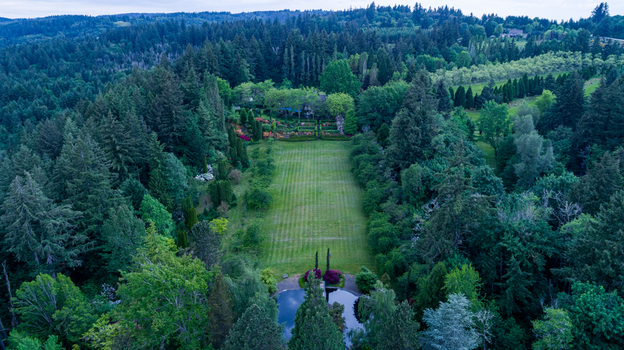 Aerial view of Northwest Skyline Boulevard area featuring a long green lawn surrounded by dense evergreen forest and a small pond in Portland Oregon United States. Aerial view of Northwest Skyline Boulevard area featuring a long green lawn surrounded by dense evergreen forest and a small pond in Portland Oregon United States.