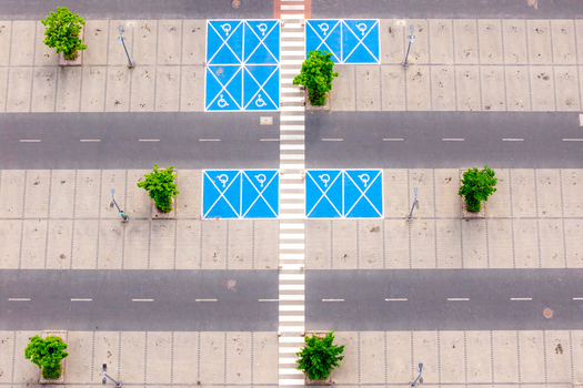Aerial view of a large parking lot with blue handicap parking spaces white pedestrian crosswalks and green trees in Warsaw Masovian Voivodeship Poland. Aerial view of a large parking lot with blue handicap parking spaces white pedestrian crosswalks and green trees in Warsaw Masovian Voivodeship Poland.