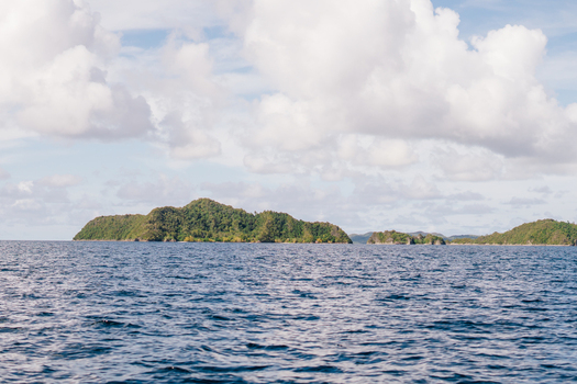 View of Raja Ampat islands with lush green vegetation surrounded by deep blue sea under a cloudy sky in Southwest Papua Indonesia. View of Raja Ampat islands with lush green vegetation surrounded by deep blue sea under a cloudy sky in Southwest Papua Indonesia.