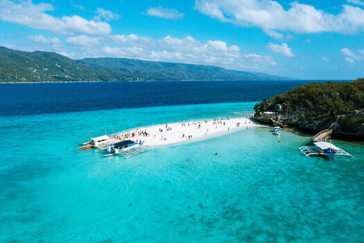 Aerial view of the white sandbar surrounded by turquoise water with outrigger boats and people walking on the beach in Oslob Central Visayas Philippines. Aerial view of the white sandbar surrounded by turquoise water with outrigger boats and people walking on the beach in Oslob Central Visayas Philippines.
