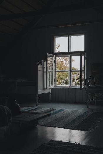 Laane County Estonia 02 June 2024 View of a rustic room with an open window looking out onto lush foliage featuring a wooden bed frame a patterned rug and soft natural light.