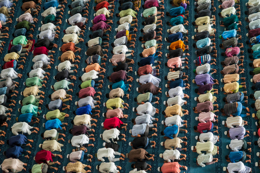 Dhaka Bangladesh 19 June 2026 Aerial view of many men praying in rows inside a mosque with colorful traditional clothing and patterned prayer mats on the floor.