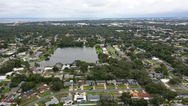 Aerial view of a residential neighborhood featuring a central lake surrounded by suburban houses and lush greenery under a cloudy sky in Clearwater Florida United States.