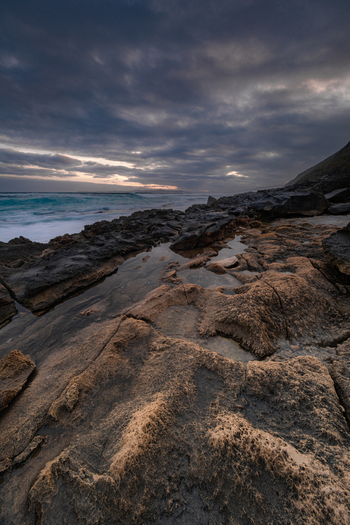 View of the rugged rocky coastline at Sandpatch during dusk with dark clouds over the ocean and tide pools in the foreground Sandpatch Western Australia Australia. View of the rugged rocky coastline at Sandpatch during dusk with dark clouds over the ocean and tide pools in the foreground Sandpatch Western Australia Australia.
