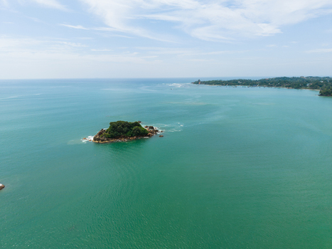 Aerial view of Taprobane Island surrounded by turquoise ocean water and the lush coastline under a bright sky in Weligama Southern Province Sri Lanka.