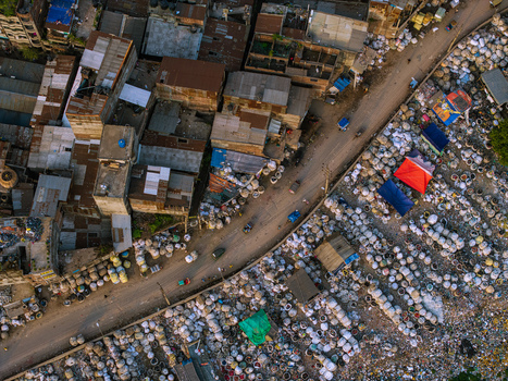 Aerial view of a busy street and dense urban buildings next to a large waste sorting area with white sacks and colorful tarps in Keraniganj Dhaka Division Bangladesh. Aerial view of a busy street and dense urban buildings next to a large waste sorting area with white sacks and colorful tarps in Keraniganj Dhaka Division Bangladesh.