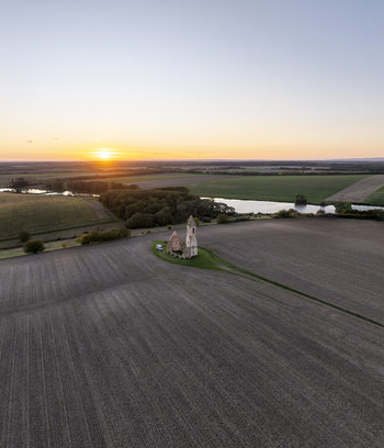 Aerial view of the historic Pusztatorony ruins surrounded by vast agricultural fields and a small pond under a golden sunset sky in Somogyvamos Hungary. Aerial view of the historic Pusztatorony ruins surrounded by vast agricultural fields and a small pond under a golden sunset sky in Somogyvamos Hungary.