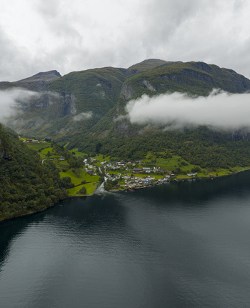 Aerial view of the village of Undredal nestled at the base of steep mountains along the Aurlandsfjord with low clouds and lush green slopes Undredal Vestland Norway.