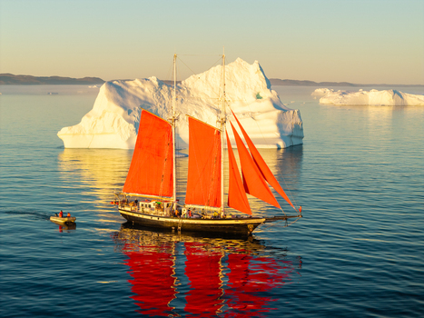Aerial view of a schooner with vibrant red sails sailing through calm waters near a massive iceberg under a clear sky Greenland. Aerial view of a schooner with vibrant red sails sailing through calm waters near a massive iceberg under a clear sky Greenland.